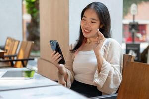 ein heiter asiatisch Frau genießt reden auf ein Anruf während chillen beim ein Restaurant im das Stadt. foto