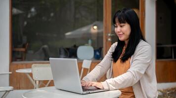 ein Frau ist Arbeiten entfernt beim ein draussen Tabelle von ein Cafe, reagieren zu E-Mails auf ihr Laptop. foto