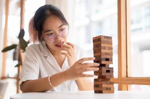 ein jung asiatisch Frau Fokussierung auf spielen ein hölzern Block Spiel beim ein Tabelle drinnen. foto