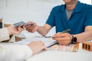 ein Klient ist Unterzeichnung ein Haus Gebäude Versicherung Vertrag und bezahlen Geld zu ihr Auftragnehmer. foto