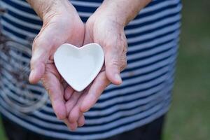 Nahansicht Schuss von ein herzförmig Weiß Keramik auf das Palme von ein Senior Frau. Valentinstag Tag. Raum zum Text. Konzept von alt Menschen und Gesundheitswesen foto