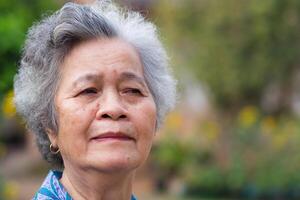 Porträt von Alten Frau mit kurz Weiß Haar und Stehen Lächeln im Garten. asiatisch Senior Frau gesund und haben positiv Gedanken auf Leben machen ihr glücklich jeder Tag. Gesundheit Pflege Konzept foto