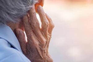 zurück Aussicht von Alten Frau Hand berühren im das Ohr ihr. Fokus auf Hände faltig Haut. Raum zum Text. Konzept von alt Menschen und Gesundheitswesen foto