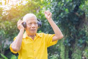 Senior Mann Stehen tragen kabellos Kopfhörer Hören zu ein Liebling Lied, und lächelnd während Stehen im ein Garten. Raum zum Text. Konzept von alt Menschen und Entspannung foto