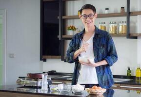 jung Mann Koch tragen beiläufig Stoff im das Küche. jung Mann Arbeiter Verwendet Schneebesen und Schüssel zum Herstellung Mischen Zutaten im ein Schüssel. Küche Werkzeuge und Kochen Konzept foto