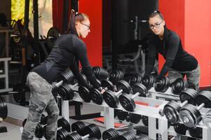 schön Mädchen mit Hände auf Hanteln suchen auf ihr Betrachtung im das Spiegel im ein Sport Halle. schlank jung Frau ist nehmen Hanteln im Vorderseite von ein Spiegel im Fitness Verein foto