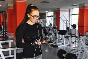 jung lächelnd Frau Hören zu Musik- auf Smartphone beim das Fitnessstudio foto