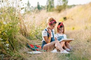 Mutter unterrichtet Tochter Farbe im Park. sonnig Natur, Mama und Tochter Farbe ein Bild im ein Park , Gemälde ein wenig Kind, Kind Kreativität. Mutter Tag. foto