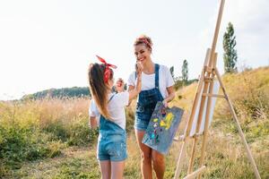 Mutter unterrichtet Tochter Farbe im Park. sonnig Natur, Mama und Tochter Farbe ein Bild im ein Park , Gemälde ein wenig Kind, Kind Kreativität. Mutter Tag. foto