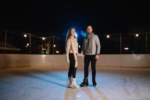 Winter Rollschuhe, liebend Paar halten Hände und rollen auf Eisbahn. Erleuchtung im Hintergrund, Nacht. Konzept Ausbildung. foto