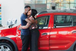 lächelnd afrikanisch amerikanisch Paar umarmen und lächelnd beim Kamera beim Neu Auto Ausstellungsraum foto