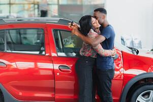 lächelnd afrikanisch amerikanisch Paar umarmen und lächelnd beim Kamera beim Neu Auto Ausstellungsraum foto