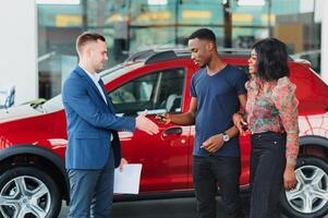 lächelnd afrikanisch amerikanisch Paar umarmen und lächelnd beim Kamera beim Neu Auto Ausstellungsraum foto