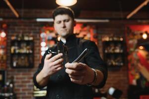 Porträt von gut aussehend jung Mann Stehen beim Barbier Geschäft. stilvoll Friseur Stehen im seine Salon mit seine Waffen gekreuzt. foto