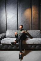 gut aussehend jung afrikanisch amerikanisch Mann im elegant passen mit Glas von Whiskey entspannend auf Sofa foto