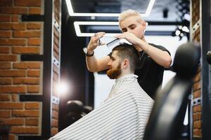 Herstellung Haarschnitt aussehen perfekt. jung bärtig Mann bekommen Haarschnitt durch Friseur während Sitzung im Stuhl beim Friseurladen. foto