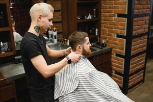 Herstellung Haarschnitt aussehen perfekt. jung bärtig Mann bekommen Haarschnitt durch Friseur während Sitzung im Stuhl beim Friseurladen. foto