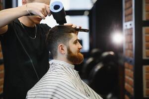 Herstellung Haarschnitt aussehen perfekt. jung bärtig Mann bekommen Haarschnitt durch Friseur während Sitzung im Stuhl beim Friseurladen. foto