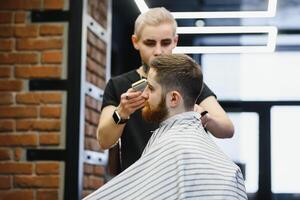 Herstellung Haarschnitt aussehen perfekt. jung bärtig Mann bekommen Haarschnitt durch Friseur während Sitzung im Stuhl beim Friseurladen. foto