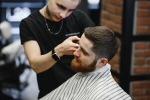 jung gut aussehend Barbier Herstellung Haarschnitt von attraktiv bärtig Mann im Friseurladen. foto