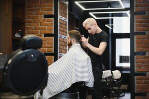 jung gut aussehend Barbier Herstellung Haarschnitt von attraktiv bärtig Mann im Friseurladen. foto