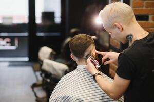 Herstellung Haarschnitt aussehen perfekt. jung bärtig Mann bekommen Haarschnitt durch Friseur während Sitzung im Stuhl beim Friseurladen. foto