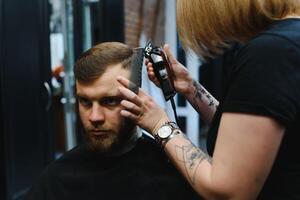 Fachmann Friseur Frau tun Styling von gut aussehend Kerl mit elektrisch Haar Clipper beim Barbier Geschäft. foto