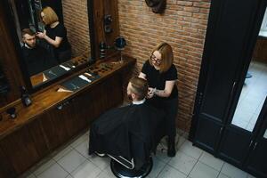 stilvoll Mann Sitzung Barbier Geschäft Friseur Friseur Frau Schneiden seine Haar Porträt gut aussehend glücklich jung bärtig kaukasisch Kerl bekommen modisch Haarschnitt attraktiv Barbier Mädchen Arbeiten Portion Klient. foto