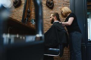 stilvoll Mann Sitzung Barbier Geschäft Friseur Friseur Frau Schneiden seine Haar Porträt gut aussehend glücklich jung bärtig kaukasisch Kerl bekommen modisch Haarschnitt attraktiv Barbier Mädchen Arbeiten Portion Klient. foto