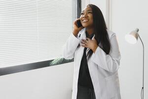 lächelnd weiblich Arzt mit Handy, Mobiltelefon Telefon im das Krankenhaus foto