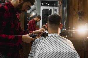 gut aussehend bärtig Mann ist lächelnd während haben seine Haar Schnitt durch Friseur beim das Friseurladen. foto