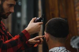 Herstellung Haarschnitt aussehen perfekt. jung bärtig Mann bekommen Haarschnitt durch Friseur während Sitzung im Stuhl beim Friseurladen. foto