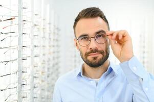 Mann wählt Brille zum Vision Korrektur im ein Augenheilkunde Salon. Brille zum Vision Korrektur foto