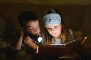 glücklich Familie Kinder lesen ein Buch mit ein Taschenlampe im ein Zelt beim Zuhause foto