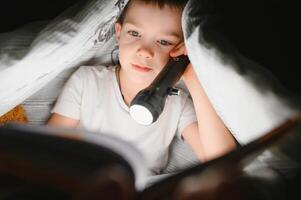 Junge mit Taschenlampe lesen Buch unter Decke beim heim. foto