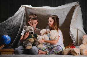 lesen und Familie Spiele im Kinder- Zelt. Junge und Mädchen mit Buch und Taschenlampe Vor gehen zu Bett foto