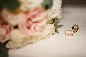 Gold Ringe und ein schön Braut- Strauß von Rosen auf das Hintergrund. Einzelheiten, Hochzeit Traditionen. Nahaufnahme, Makro. foto