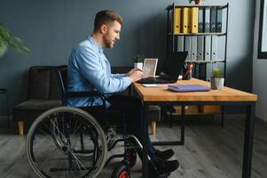 jung glücklich Unternehmer im Rollstuhl Arbeiten auf Laptop beim Zuhause foto