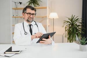 Senior Arzt mit seine Tablette Computer beim Arbeit foto