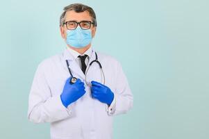 Porträt von ein männlich Arzt im ein Maske und Handschuhe auf ein Blau Hintergrund. Gesundheitswesen Konzept foto