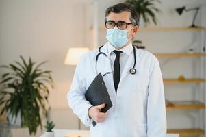 männlich Arzt mit medizinisch Gesicht Maske und ein Stethoskop beim Klinik foto