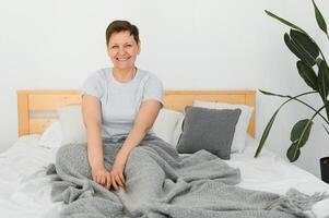 glücklich frisch schön reifen älter Frau Erwachen nach gesund Schlaf strecken aufwachen oben im gemütlich komfortabel Bett, lächelnd Mitte alt Dame genießen gut Morgen suchen beim Kamera, schließen oben Porträt, oben Sicht. foto