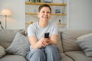 Porträt von glücklich älter Frau Ändern Kanal auf Fernsehen. foto