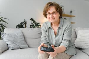 ein höchst emotional älter Dame sitzt auf das Couch beim Zuhause und Theaterstücke Spiele. Oma Gewinnt während Sitzung allein beim heim. foto