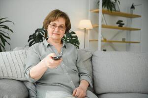 Technologie, Fernsehen, Alter und Menschen Konzept - - glücklich Senior Frau Aufpassen Fernseher und Ändern Kanal mit Fernbedienung Steuerung beim Zuhause foto