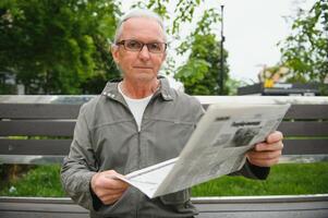 Porträt von Senior Mann lesen auf Bank während Sommer- Tag. foto