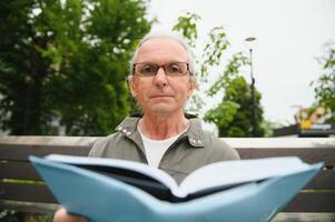 Senior Mann lesen ein Buch im das Park. foto