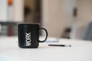 Tasse von Kaffee mit Inschrift Arbeit auf Weiß hölzern Tabelle im Büro foto