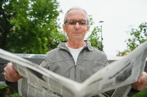 Porträt von Senior Mann lesen auf Bank während Sommer- Tag. foto