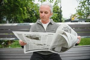 Porträt von Senior Mann lesen auf Bank während Sommer- Tag. foto